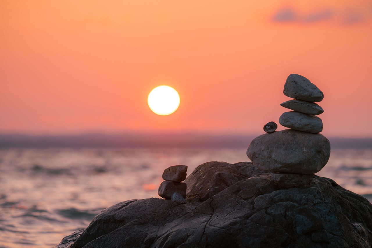 A tranquil sunset scene with balanced stones by a calm lake, exuding peace.