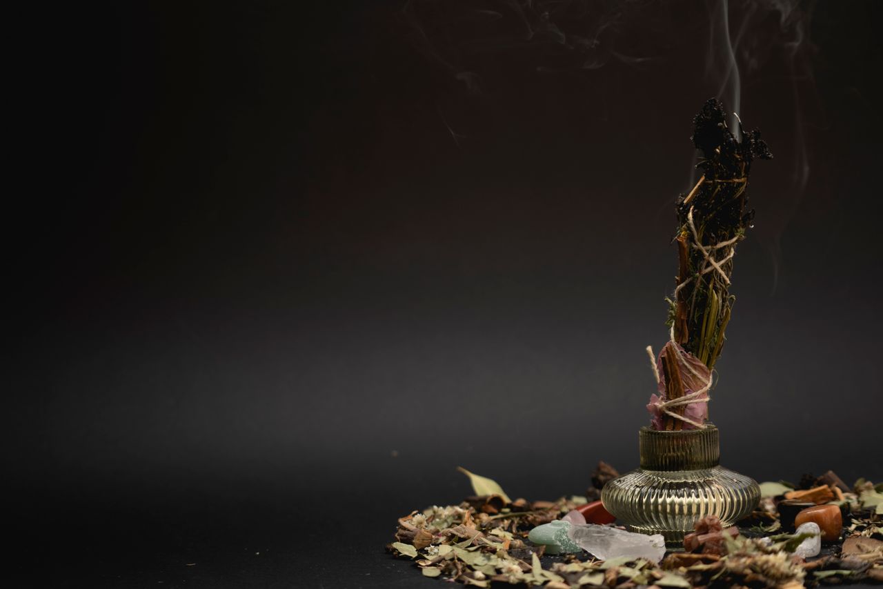 A contemplative still life of burning sage and herbs emitting smoke on a dark backdrop.